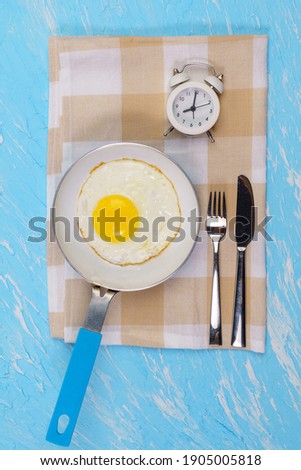 alarm clock and scrambled eggs on a blue background. for good morning