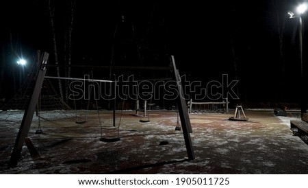 Night view of children playground and lanterns. Action. Empty winter playground with swings and sports equipment on black sky background. 
