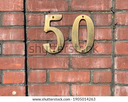 Brass number 50 on red brick wall, weathered gold tone metal house sign, street number fifty 