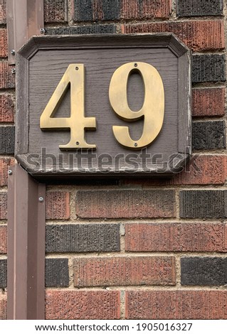 Brass house number 49 plaque on brown brick wall, sepia brownstone feel with classic Victorian and Dickensian mood, street address sign