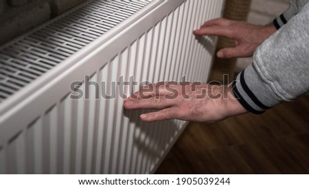 A man froze in his hands, a man warms his hands near a heating radiator, an elderly man warms his hands near an electric fireplace Royalty-Free Stock Photo #1905039244