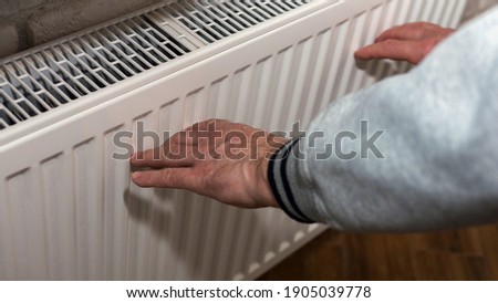 An elderly man warms his hands near a heating radiator, a man froze, a man warms himself near a fireplace. A man warms himself up by an electric battery Royalty-Free Stock Photo #1905039778