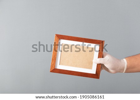Hand in a white medical glove, clutching wooden photo box. Concept of sending security mail items sending virus or coronavirus quarantine. Delivery.