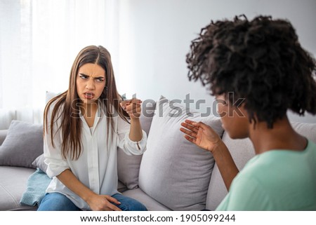 Two female friends sitting on sofa and arguing with each other. Friendship, quarrel, female disagreement, copy space. Two female friends sitting on sofa and arguing with each other. 