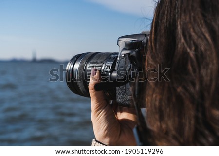 Closeup of a woman taking a photo of the Statue of Liberty from Battery Park