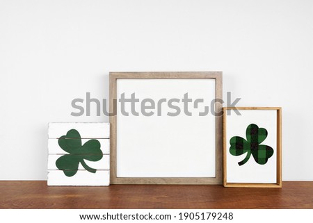 Mock up wood frame with St Patricks Day decor on a wood shelf. Rustic wood signs. Square frame against a white wall. Copy space.