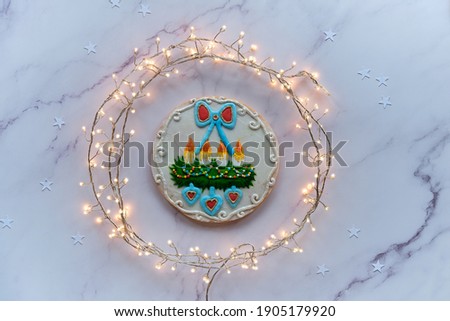 Gingerbread decorated with advent wreath with candles and hearts. Creative traditional gifts for children. Christmas flat lay with snowflakes, garland of lights on marble table.