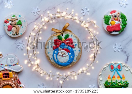 Decorated gingerbread with various motives, assortment of tasty traditional children gifts for Xmas. Christmas flat lay with festive garland in circle. Top view on white marble background.