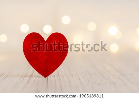 on a light wooden background a red heart, in the background the garland is out of focus