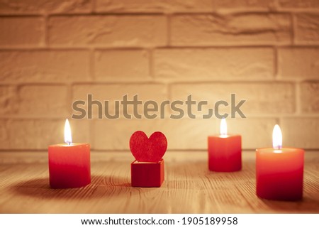 against the white brick wall three red burning candles and a box with a red heart