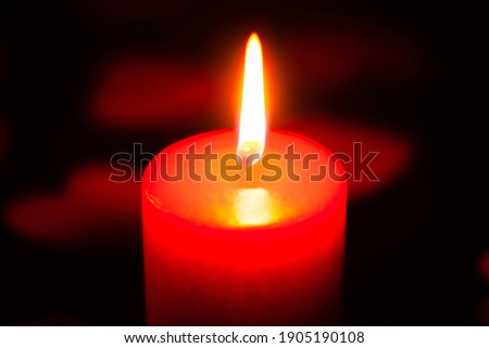 red burning candle on a black background, scattered around red hearts