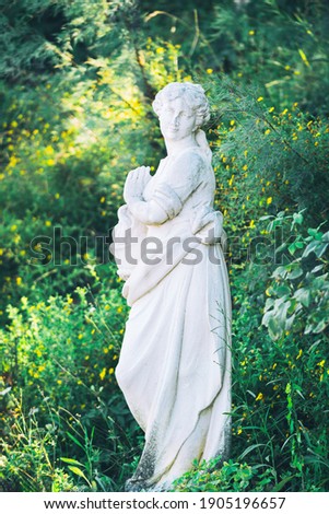 White marble sculpture of young woman antique style. Vintage portrait on green nature backdrop. Statue of ancient greek goddess in summer park outdoor