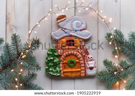 Decorated gingerbread with candles on Advent deco wreath with fir twigs. Christmas flat lay with natural fir, stars and garland of festive lights. White wooden planks, top view of rustic wood.