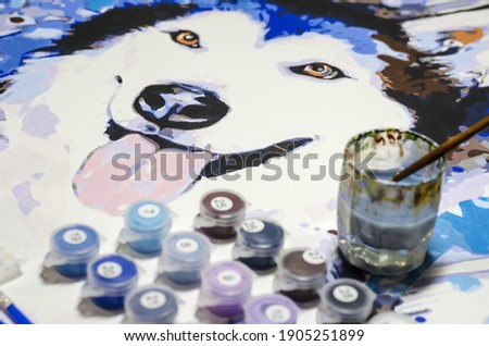 Colorful picture of husky dog on canvas, paint cans and brushes. Process of painting portrait of mischievous dog with his tongue out. Painting, art, creativity.