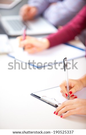 Woman at class desk signing a contract with shallow focus on pen