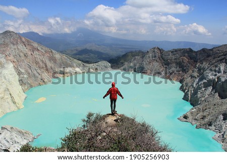 Man traveler standing on edge of crater with colorful sky at morning. Beautiful Ijen volcano with acid lake and sulfur gas going from crater, Indonesia