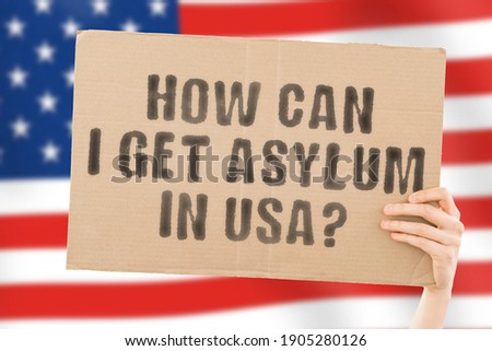 The phrase " How can I get asylum in USA " on a banner in men's hand with blurred American flag on the background. Claim. Refugee. Immigration. Law. Legislation Royalty-Free Stock Photo #1905280126