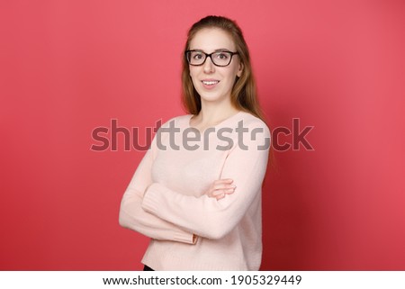 Portrait of smiling young girl in glasses with crossed arms on pink background