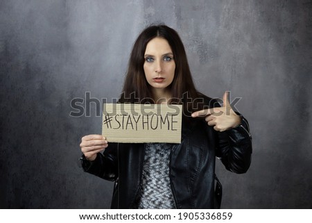 young woman holds a stay home poster on a gray background