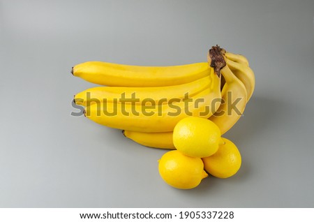 Bunch of bananas and three lemon on a gray background. Trending color of year 2021 Illuminating and Ultimate gray. Side view minimal still life.