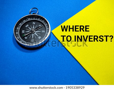 Selective focus.Text WHERE TO INVERST with compass on a blue and yellow background.Business concept.Shot were noise and film grain.