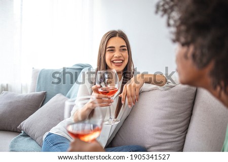 Two Female Friends Relaxing On Sofa At Home With Glass Of Wine Talking Together. Friends spending time talking and drinking wine. Shot of two friends talking together and drinking wine at home