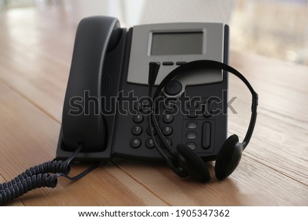 Office desktop telephone and headset on wooden table. Hotline service