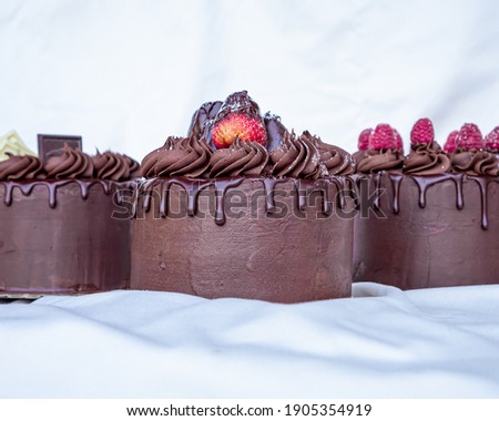Exquisite valentine's day chocolate cakes decorated with red fruits, chocolate pieces and strawberries on a table with a white tablecloth and white background.