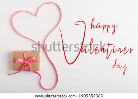 A gift of craft paper and a pink ribbon on white wooden table. Valentine's day postcard.