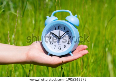 Blue alarm clock on young female hand on bright sunlight.Concept of summer time coming. 