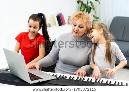 grandmother and granddaughters learn to play the piano synthesizer on a laptop online at home