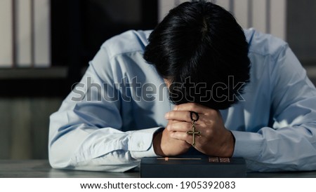 Asian man bowing his head on the Bible and carrying a cross. According to the beliefs of Christianity Is the salvation of Jesus. And pray for god protection. Concept prayer wish