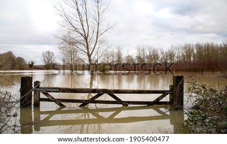 Flooded agricultural farm fields with wooden gate, sky, reflection in water, soaked field. High water in spring, UK, Suffolk spring 2021 Royalty-Free Stock Photo #1905400477