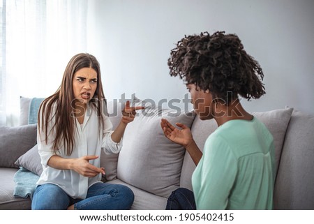 Two female friends sitting on sofa and arguing with each other. Friendship, quarrel, female disagreement, copy space. Angry friends or roommates sitting on a sofa in the living room at home Royalty-Free Stock Photo #1905402415