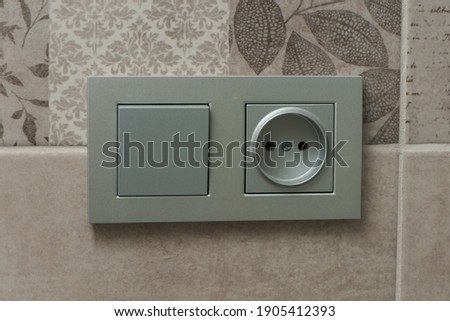 Close up view of gray European electrical outlet and switch located on gray tiles.