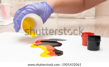 a human hand pours paint on a white sheet of paper. the paint can