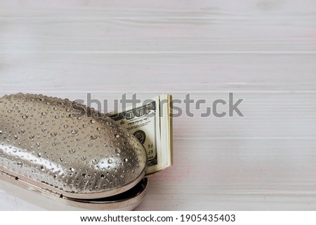 women's small handbag is open and money is visible from it. dollar bills can be seen from the clutch. evening bag on a light background. High quality photo