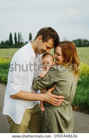 Young parents hug and kiss their newborn daughter in nature.