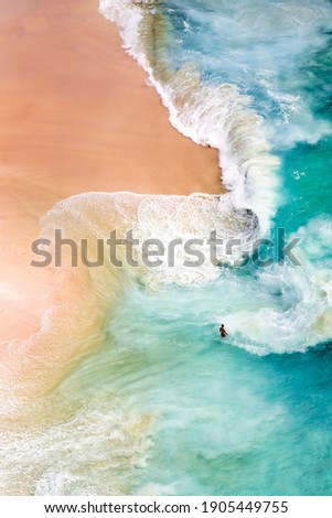 View from above, stunning aerial view of a person relaxing on a beautiful beach bathed by a turquoise sea during sunset. Kelingking beach, Nusa Penida, Indonesia. Royalty-Free Stock Photo #1905449755