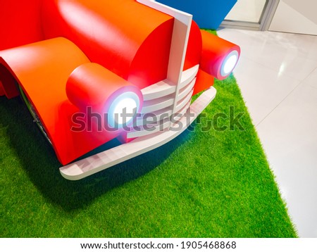 Fragment of a children's bed in the form of a car. Children's bed in the style of a cartoon car. A bed on a grass carpet. Concept - children's furniture. Furniture in a baby store.