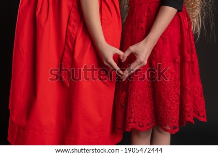Girl and baby sign love hands hold happy symbol, the design of Valentine's Day, on the floor hearts of the romance layout. February 14 art. emotions festive, black in red girl dress, barefoot