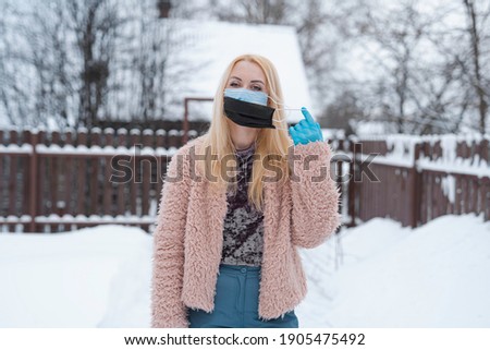 two masks. Woman removes double medical mask from face with hand in blue glove