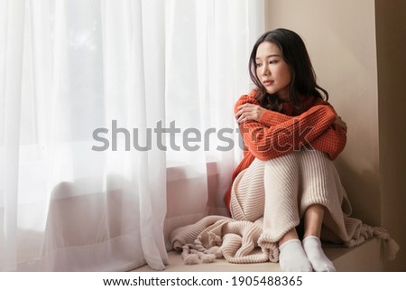 A beautiful Asian woman. young women the pensive face looking away thinking of problems sit alone at home, Sad eyes, Winter sadness Royalty-Free Stock Photo #1905488365