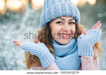Winter portrait of beautiful smiling woman with snowflakes blue gloves and knitted sweater. Model closed her eyes and hugging herself by hands, wearing stylish knitted winter hat and gloves.