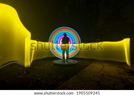 one person standing against beautiful yellow red and green circle light painting as the backdrop