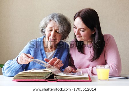 Grandmother and daughter watching a family album with old photos together - Linking generations in a common activity - An elderly and a young woman talking together-Family relations concept