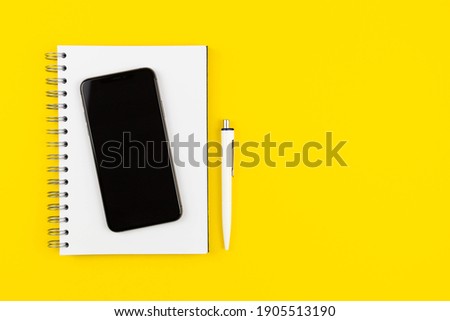 Modern office desk with smartphone with blank mockup screen, blank paper notepad on yellow background. Top view. Copy space. Flat lay.