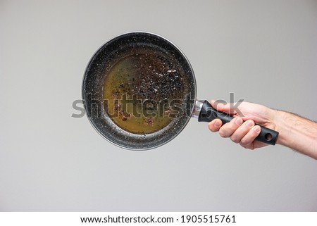 Caucasian male hand holding an old frying pan stained with brown burned oil and grease isolated on gray. Royalty-Free Stock Photo #1905515761