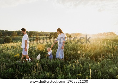 Young beautiful family with a little daughter and a dog hug, kiss and walk in nature at sunset. Royalty-Free Stock Photo #1905521230