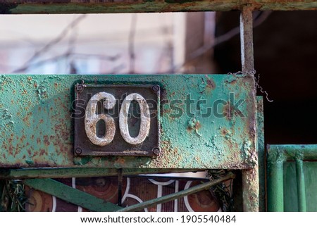 Number 60, the number of houses, apartments, streets. The white number on a brown metal plate, house number sixty (60) on a rough wall.